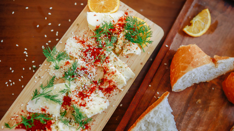 A butter board, with slices of butter spread on a cutting board enhanced by spices and herbs