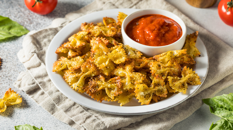 A plate of pasta chips with marinara sauce, on a towel on a table top