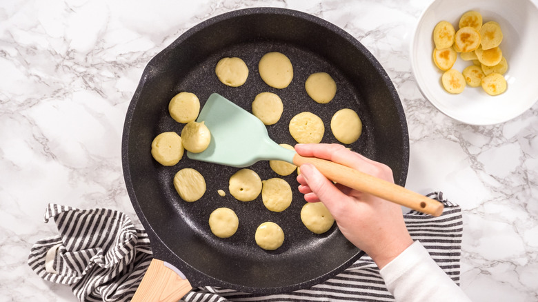 A pan of mini pancakes being cooked by a person holding a spatula