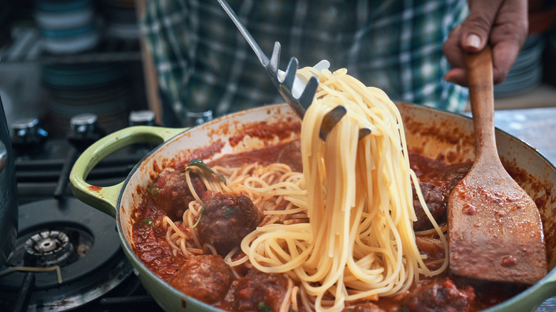 person adding pasta to sauce