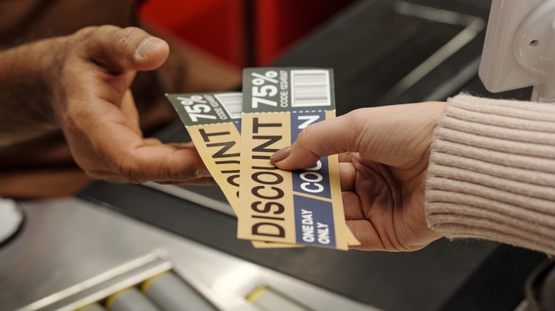 A woman hands two generic 75% off coupons to a cashier