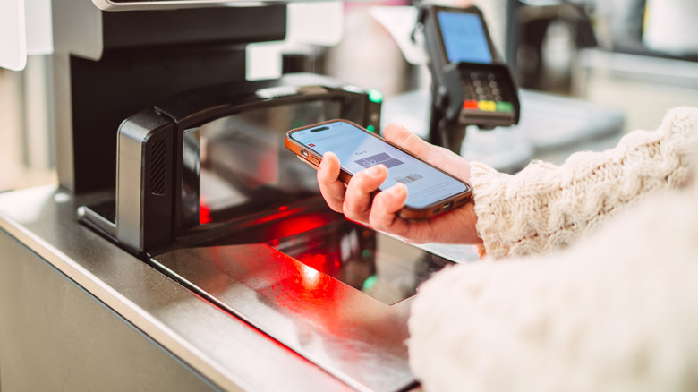 A woman is scanning a barcode on her phone at a self-checkout machine