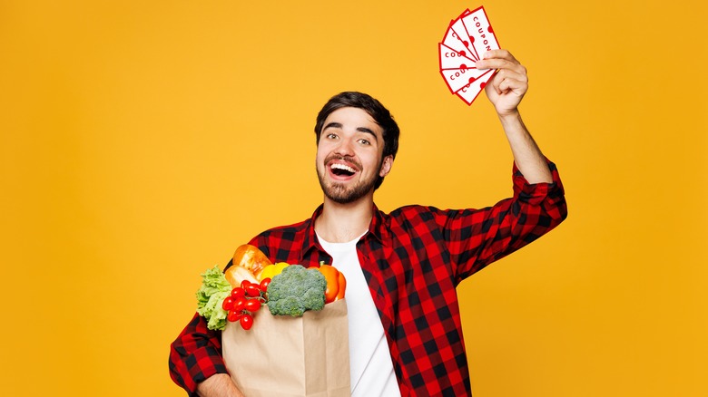 A happy man holding an overflowing bag of groceries waves a handful of generic coupons around