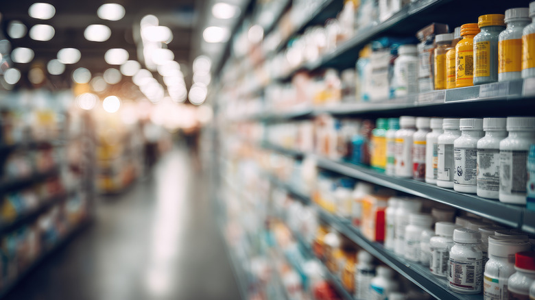 A grocery store aisle in soft focus with a focus in the foreground on bottles of vitamins