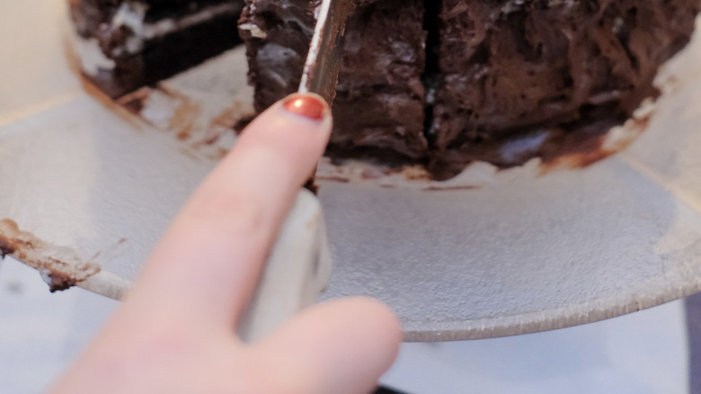 Person slicing into chocolate cake with knife
