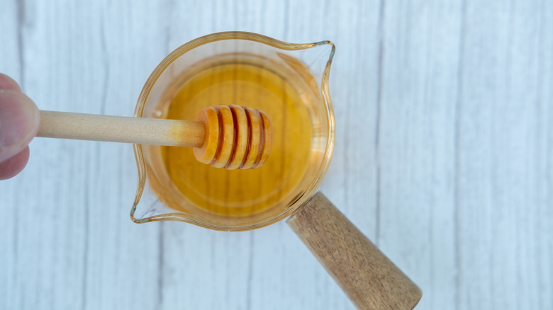 Person holding honey dipper above honey-filled measuring cup