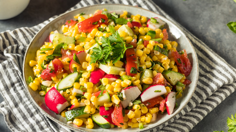 Fresh corn salad with tomato and radish on a pinstriped napkin.