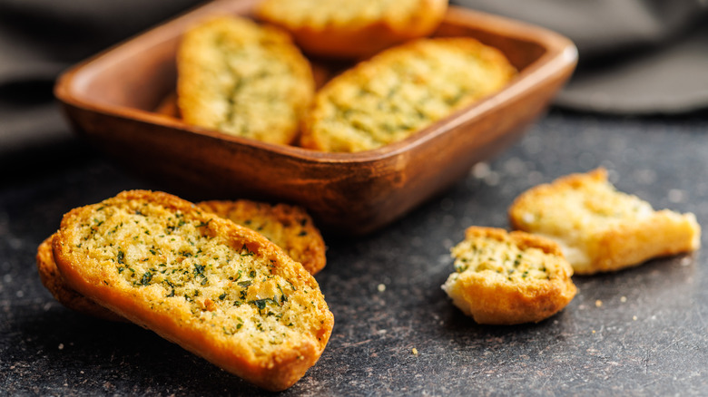 Crispy garlic bread in dish and dark counter.