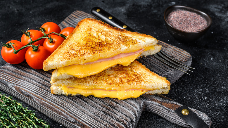 Grilled cheese sandwich with ham on wood cutting board next to fresh produce.