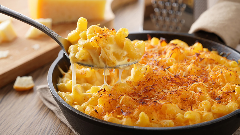 Spoon scooping macaroni and cheese out of cast iron skillet with crispy cheese on top.