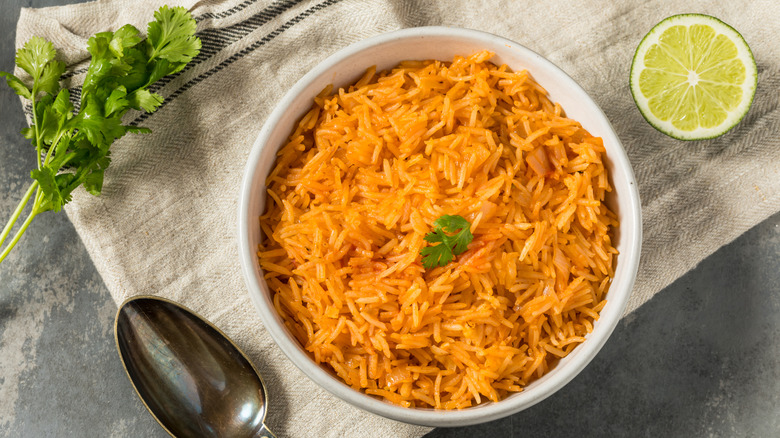 Seasoned mexican rice in white bowl next to lime and cilantro.