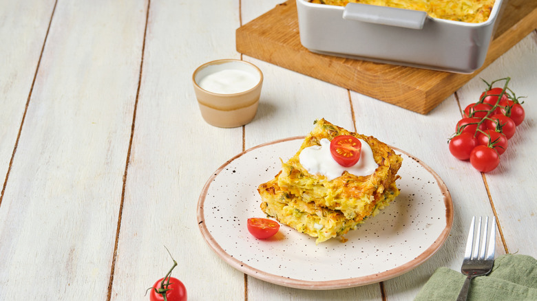 Slices of a casserole on a white plate garnished with sour cream and a tomato half