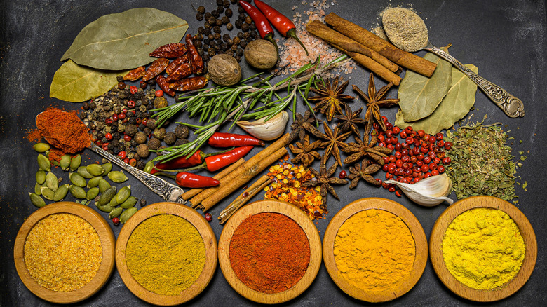 Assorted seasoning in piles and wooden bowls on a black background