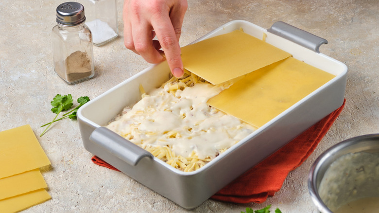 Person assembling a pasta-based casserole in a white dish
