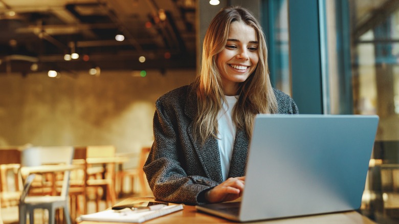 woman smiling as she looks at laptop in empty restaurant