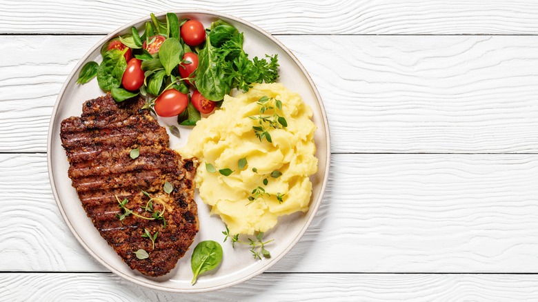 steak and potatoes with salad on white backdrop