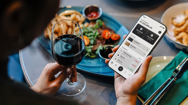 person holding glass of wine and money app on phone