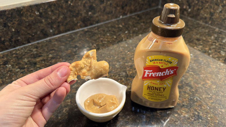 Person scooping mustard with pretzel chip