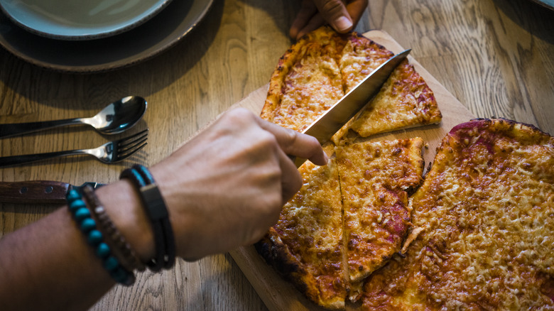 Person cutting pizza with chef's knife