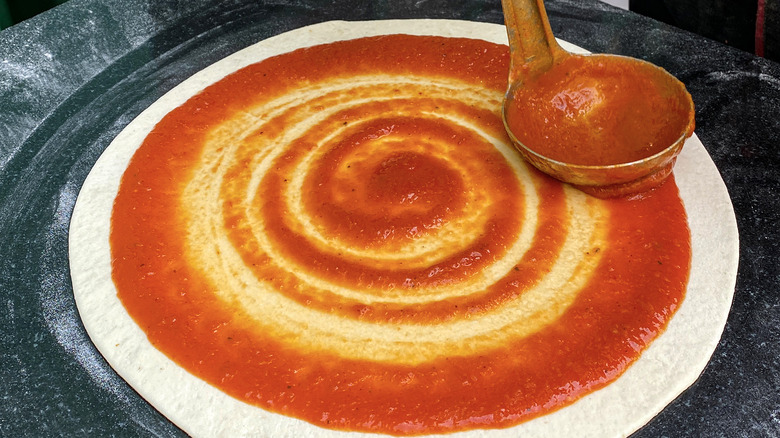 Person spreading sauce on a pizza