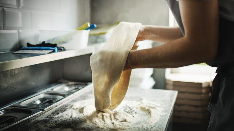 Person stretching pizza dough on a line