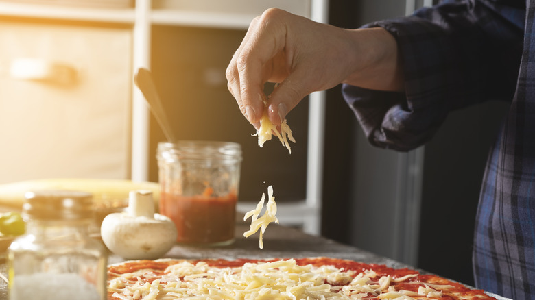 Person sprinkling cheese on pizza