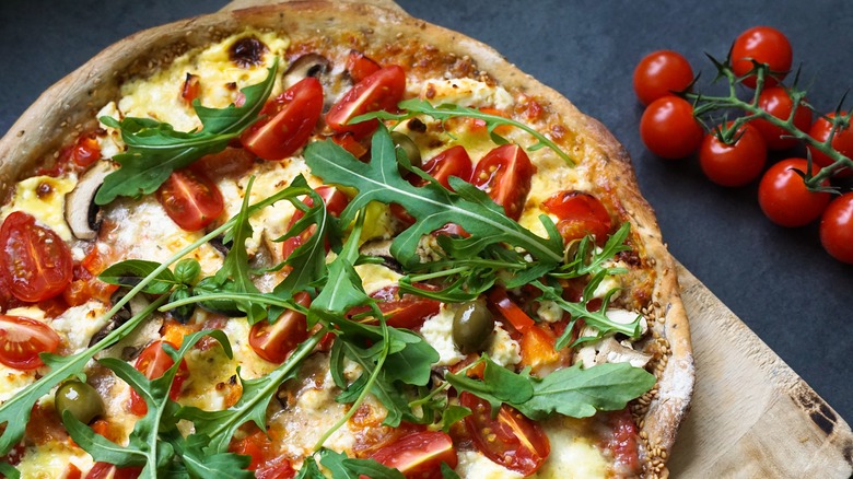 Arugula on top of a pizza with tomatoes