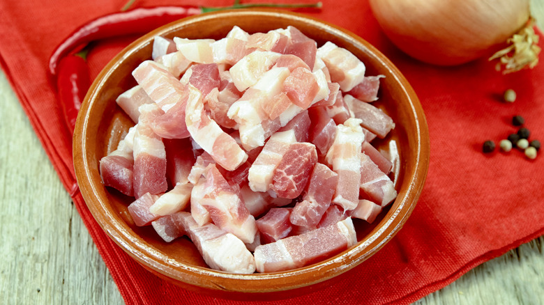 raw bacon lardons in a brown bowl with red cloth beneath it