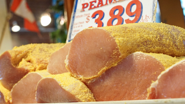 fresh slabs of peameal bacon for sale at a market with a price board behind it