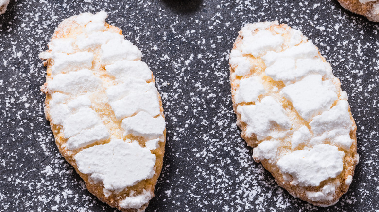 two Ricciarelli cookies covered in powdered sugar