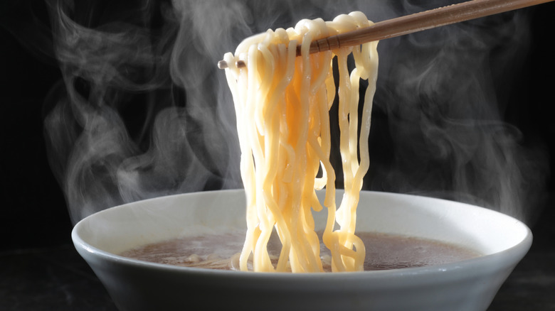 someone lifting noodles out of a hot bowl of broth with chopsticks