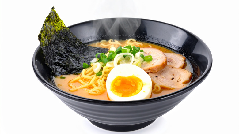 steaming black bowl of miso ramen topped with egg, noodles, scallions and nori