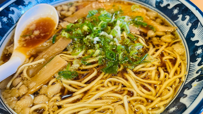 a bowl of onomichi ramen topped with a spoon and scallions