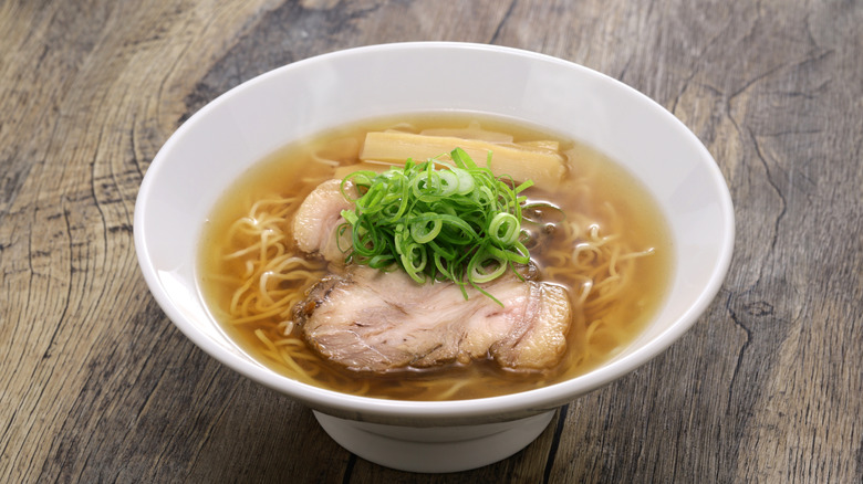 a white bowl of shoyu ramen topped with scallions that sits on a wooden table