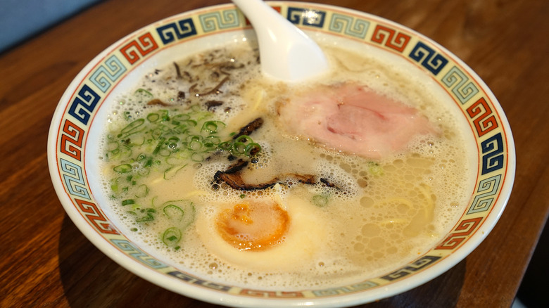 A bowl of tonkotsu ramen in a colorful patterned bowl on a wooden table.