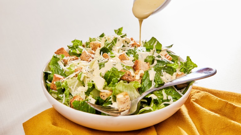 Caesar dressing being poured onto a crisp salad with croutons