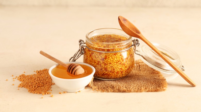 Jar of wholegrain mustard with a small bowl on honey in front