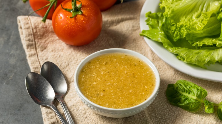 Italian dressing in white bowl,with tomatoes and salad leaves beside it