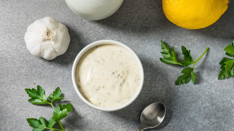 Ranch dressing in a white bowl with garlic, lemons, and parsley surrounding it