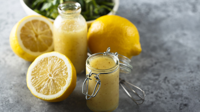 Homemade lemon vinaigrette in a small glass jar with halved lemons alongside