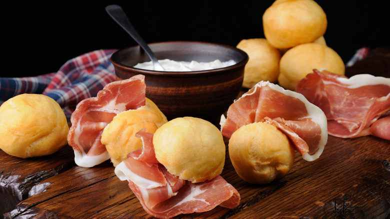 Coccoli fiorentini with prosciutto and stracchino cheese on a wooden cutting board