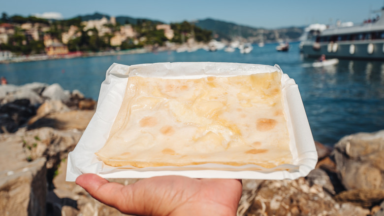 A person holding a slice of focaccia di Recco at the beach