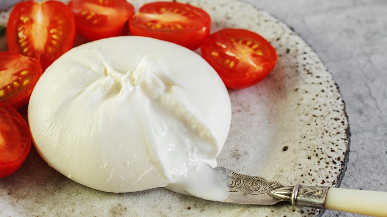 A ball of burrata cheese on a plate with tomatoes and a knife