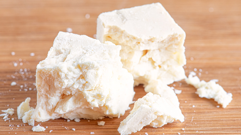 A block of feta cheese crumbled on a wooden cutting board