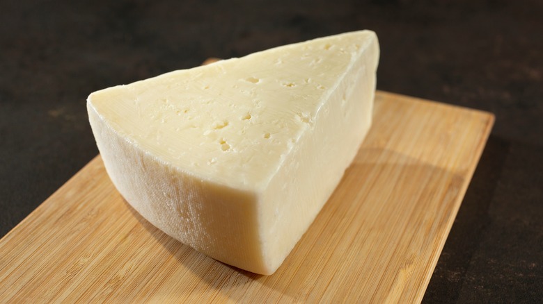 A wedge of fontina cheese on a wooden cutting board