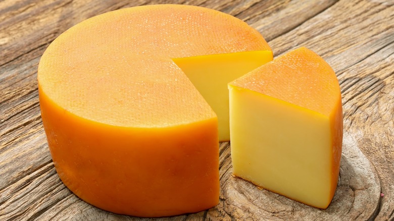 A block of smoked gouda on a cutting board with a wedge cut out