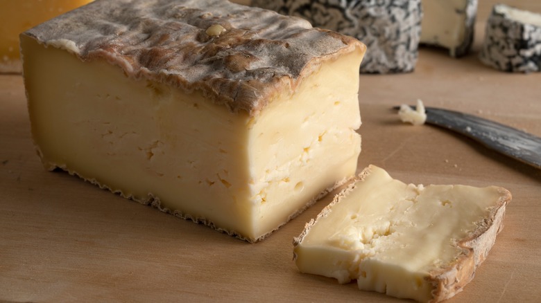 A block of Taleggio cheese on a cutting board with a slice cut off
