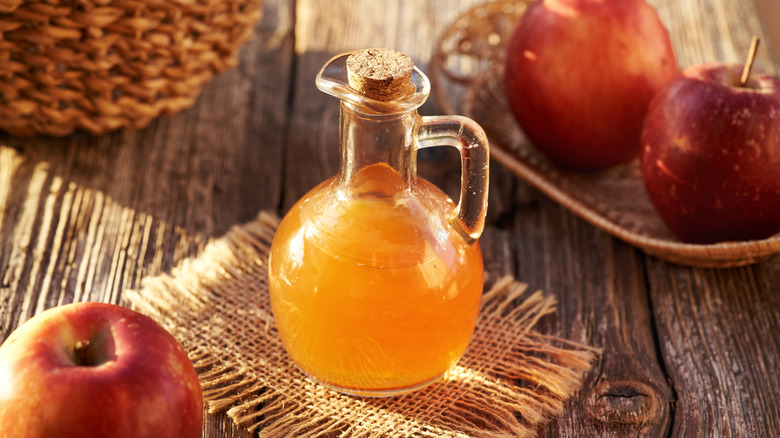 Container of apple cider vinegar besides whole apples