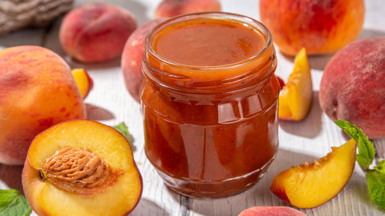 Peach jam in a jar surrounded by peaches