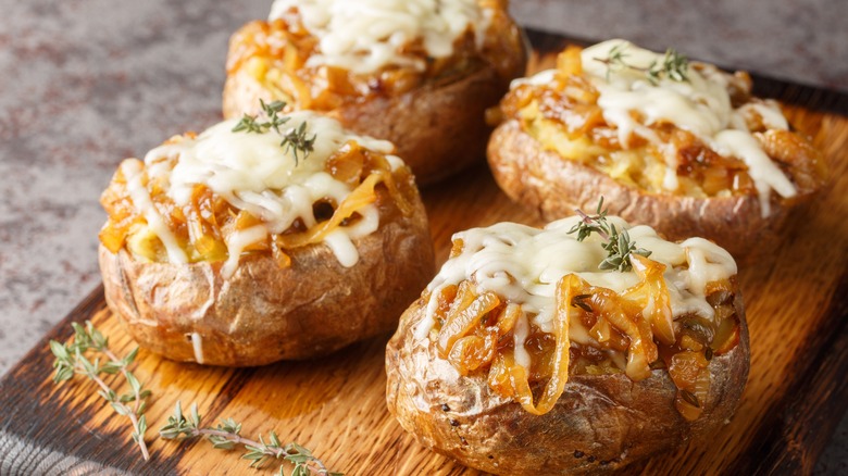 Board of small baked potatoes topped with caramelized onions and white cheese